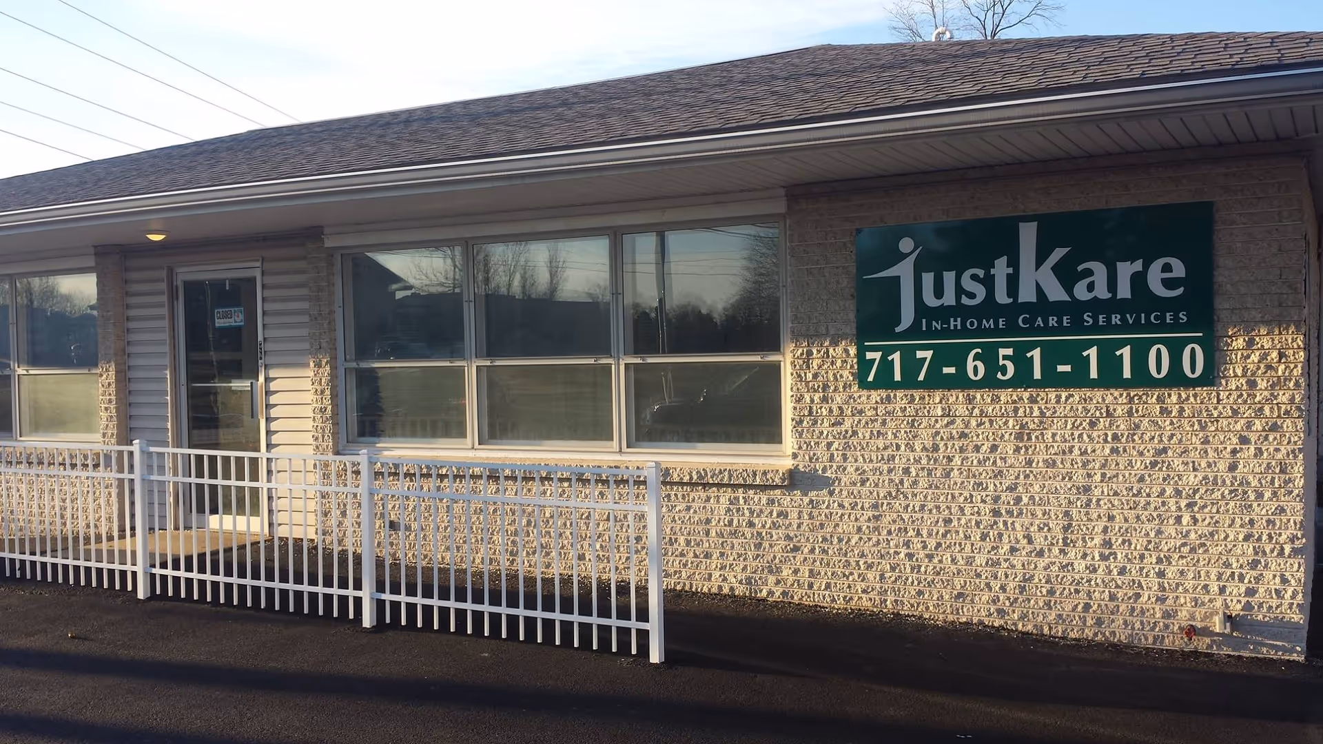 Exterior view of a beige brick building with white railing and a JustKare sign.