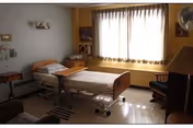 Nursing home patient bedroom featuring a bed, chair, and large window.