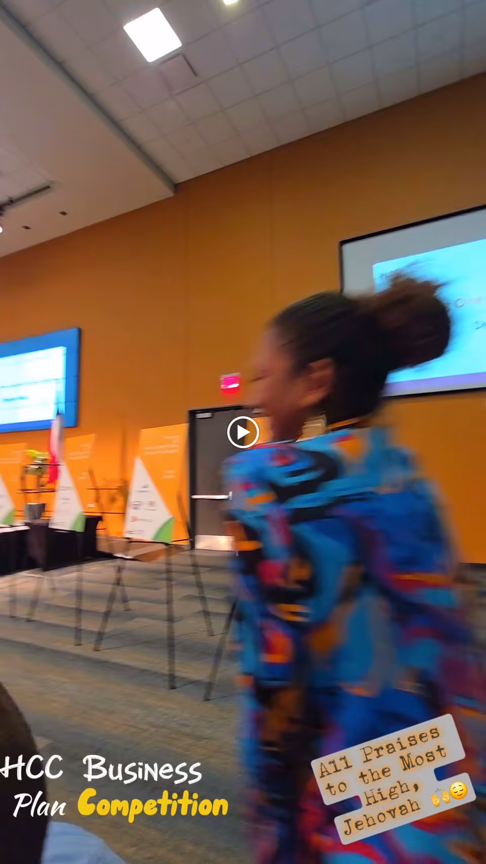 A blurred person in a colorful jacket walks through a conference room with presentation screens, easels, and signage.