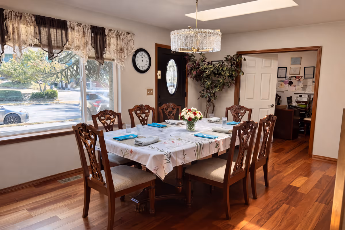 A dining room with a long table, chairs, a chandelier, and window view.
