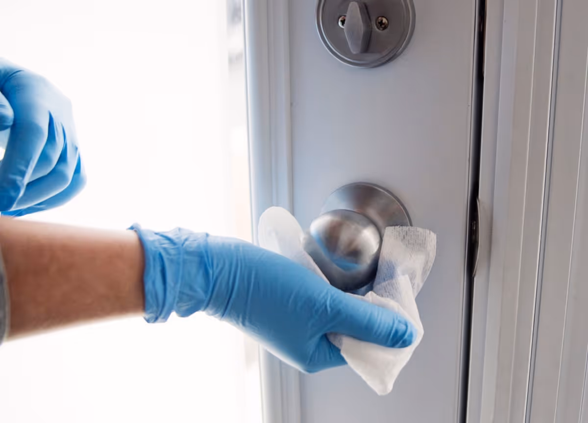 Gloved hand wipes a door handle with a white cloth inside a facility.