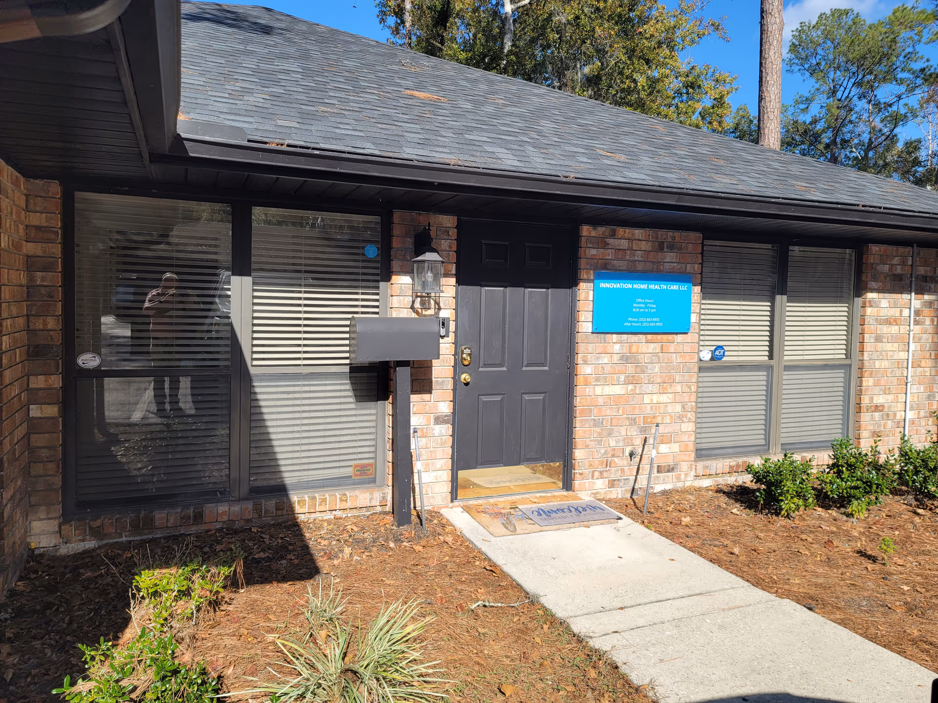 Brick facility exterior with a black front door, blue sign, and large windows.