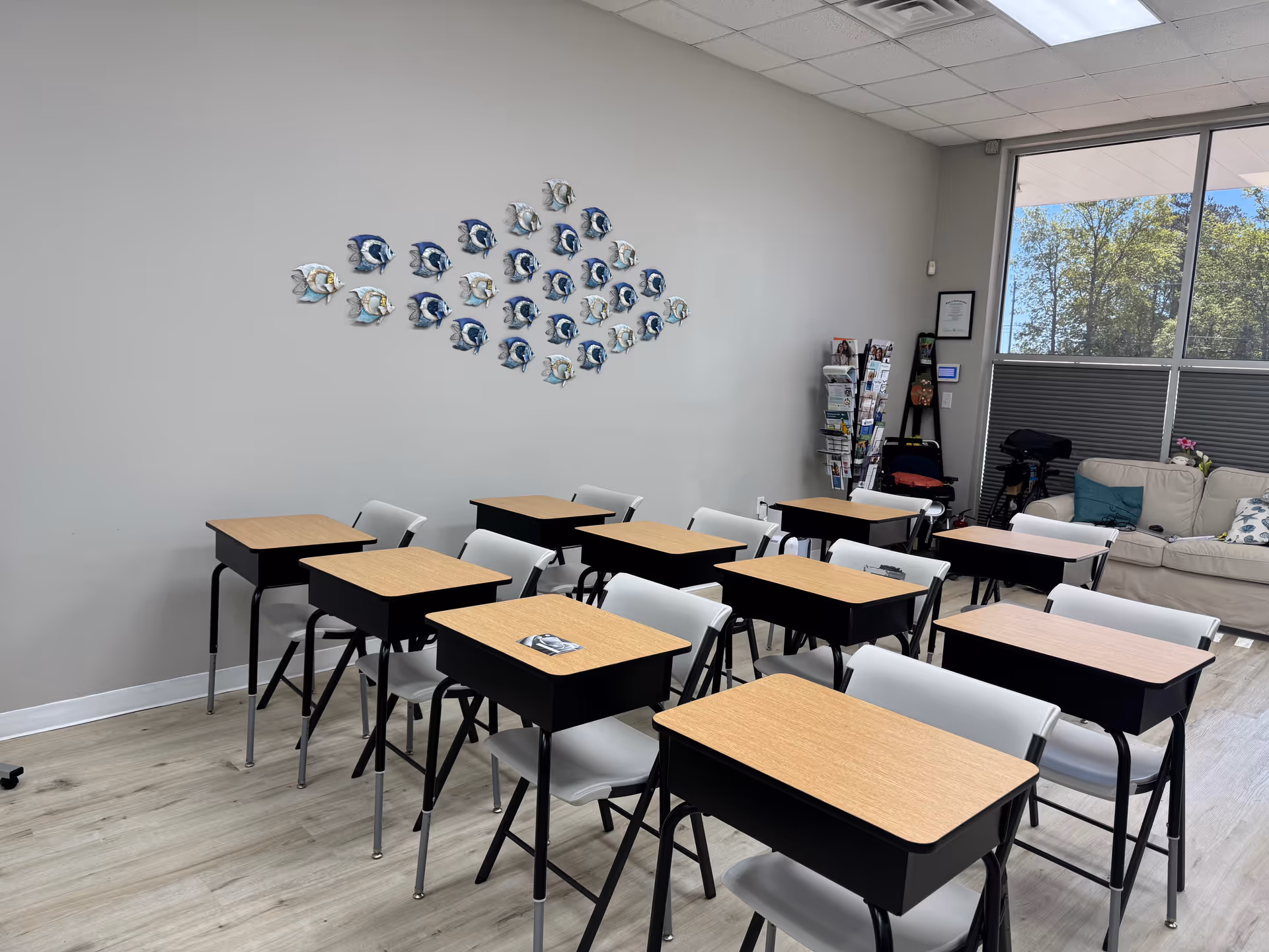 Interior classroom area with desks, white chairs, fish wall art, and a seating nook.
