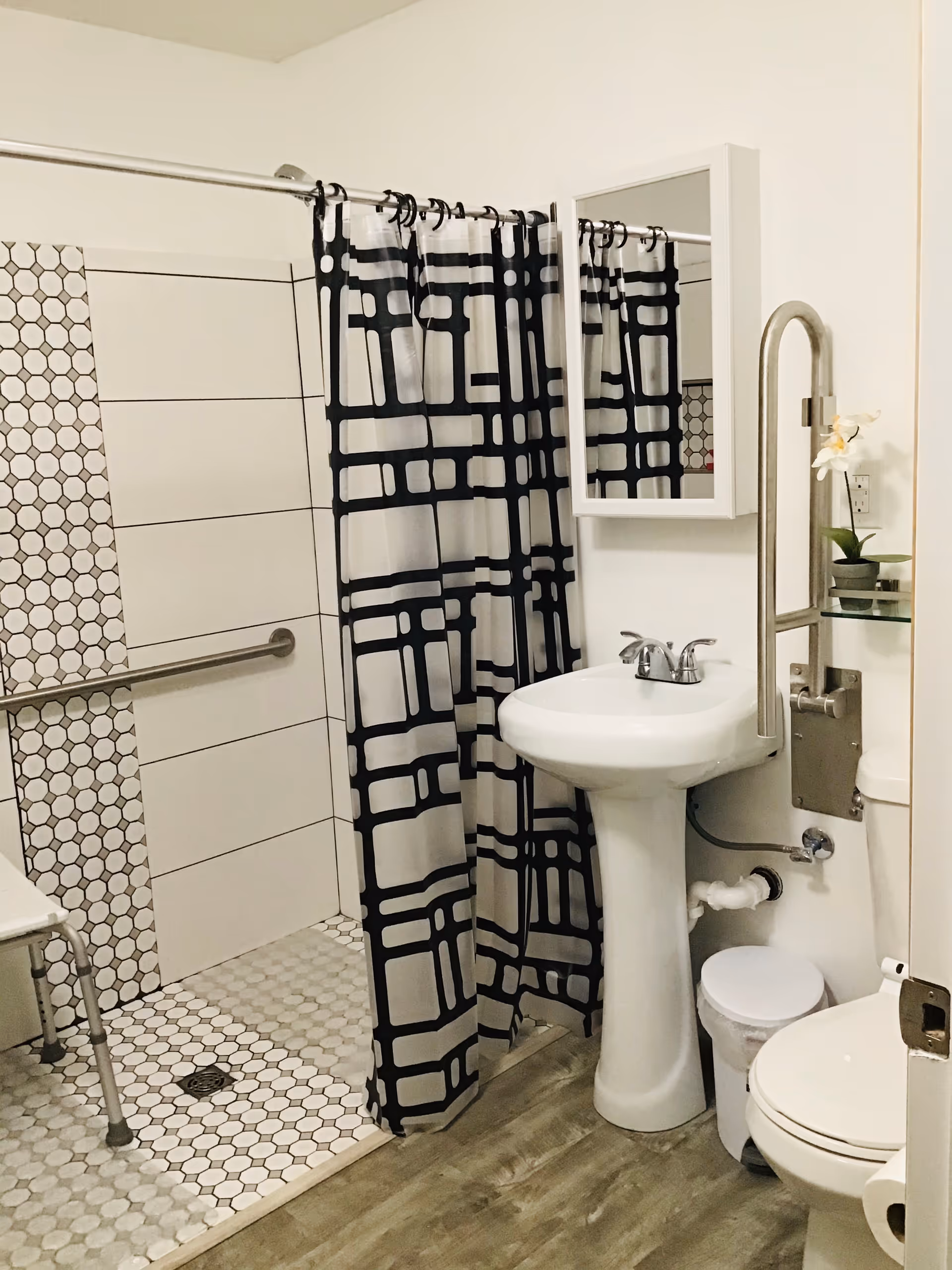 Small bathroom with pedestal sink, toilet, patterned shower curtain, and hexagonal tiled floor.