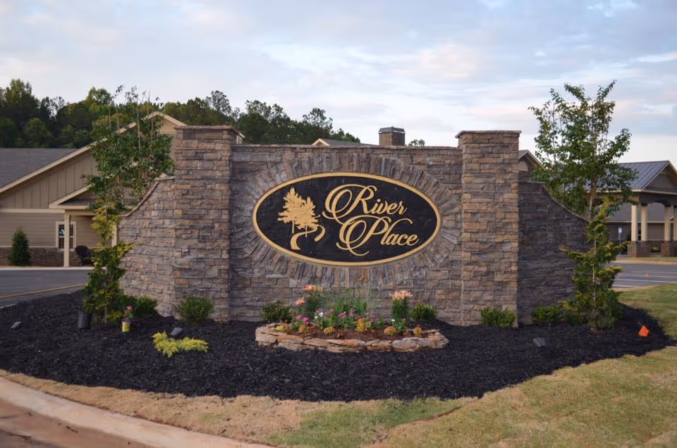 Stone sign reading River Place with landscaped front yard and surrounding campus buildings.