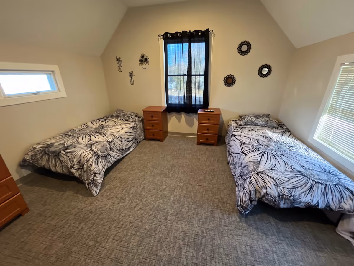 Two twin beds with black-and-white floral bedding flank a central window with two dressers.