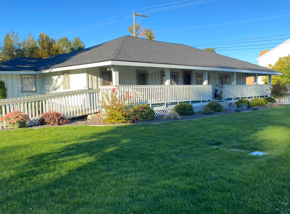 Single-story facility exterior with a long front porch, white railing, and manicured green lawn.
