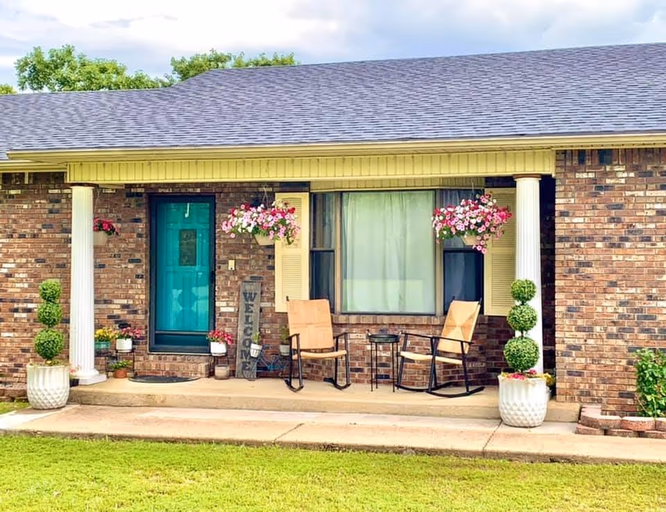 Brick-front porch of Fortress Living Care Home with chairs and hanging planters.