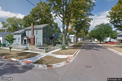 Residential street with a green house and trees along a quiet road