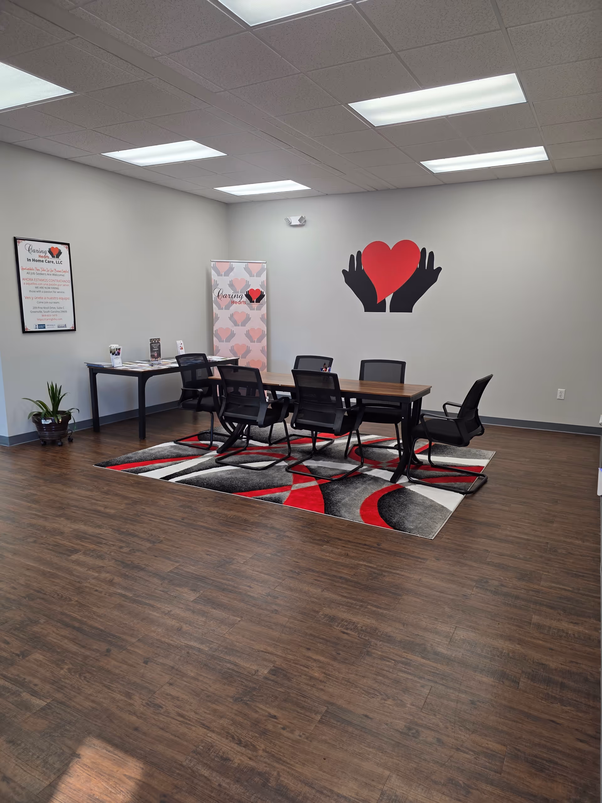 Spacious interior meeting room with a long table, black chairs, rug, and heart wall art.