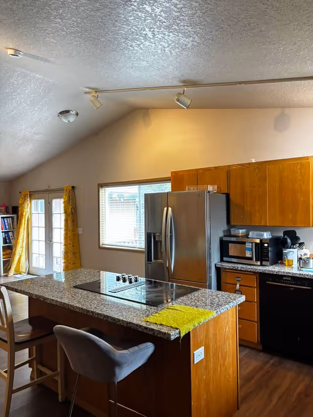 Kitchen with island, fridge, microwave, wooden cabinets, and yellow curtains in a senior living home.