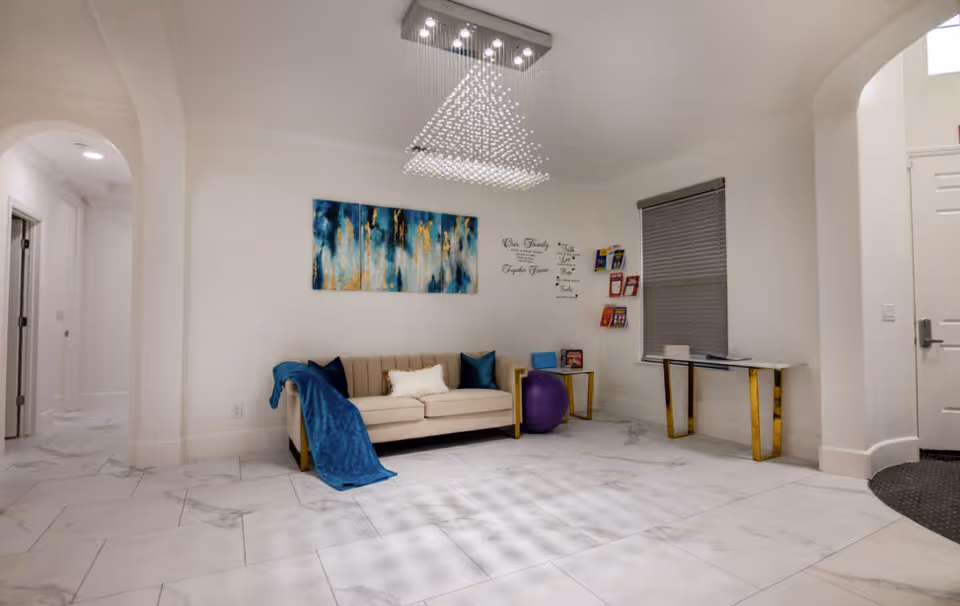 Bright modern living room-style lobby with beige sofa, artwork, chandelier, and decorative table.