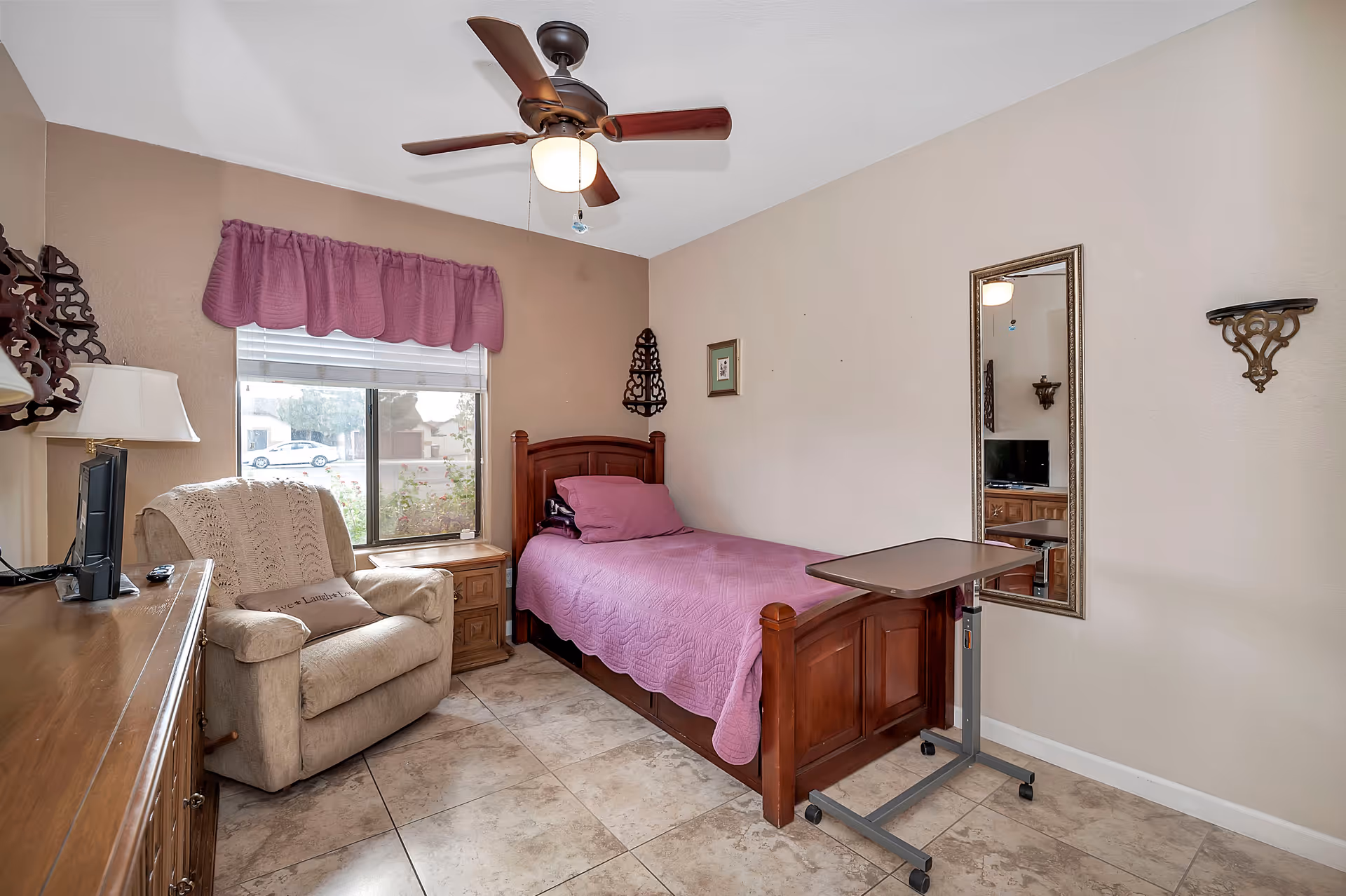 Cozy bedroom in a senior care facility with a wooden bed, dresser, and window.