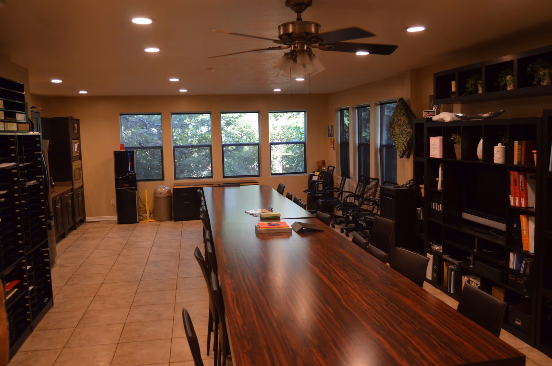 Long wooden conference table with chairs in a room lined by shelves and windows.