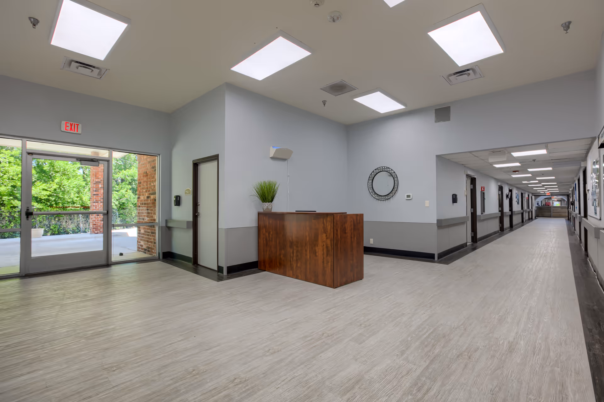 Bright, empty hallway of a senior living facility with a reception desk and glass exit doors.