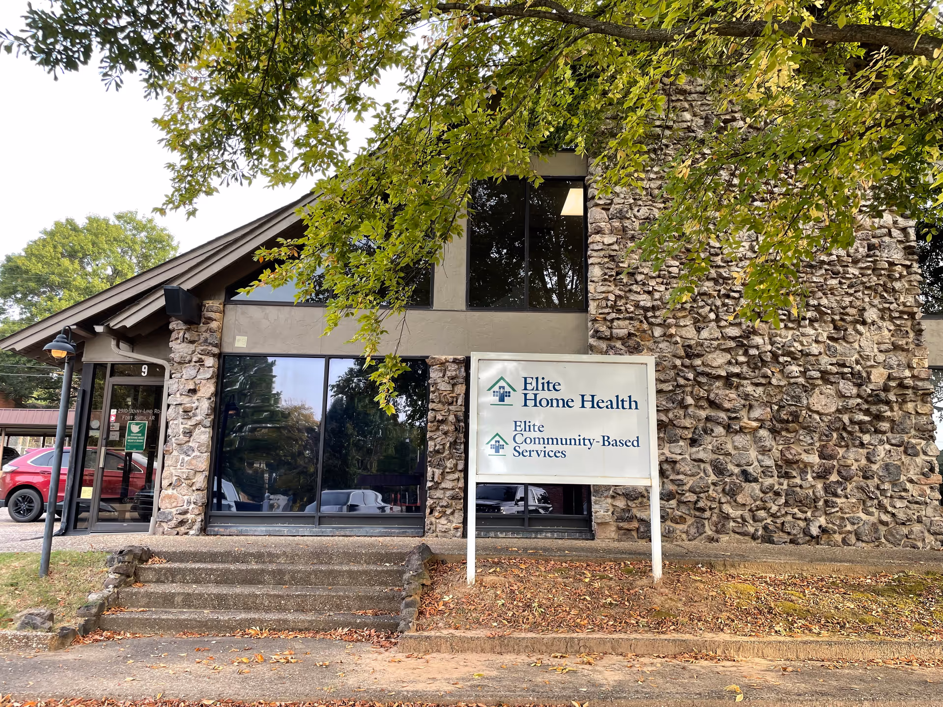 Stone facade building with glass entrance, steps, and a sign reading Elite Home Health Fort Smith.