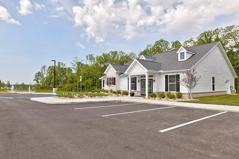 Single-story white building with a covered front entrance and an empty parking lot under a partly cloudy sky.