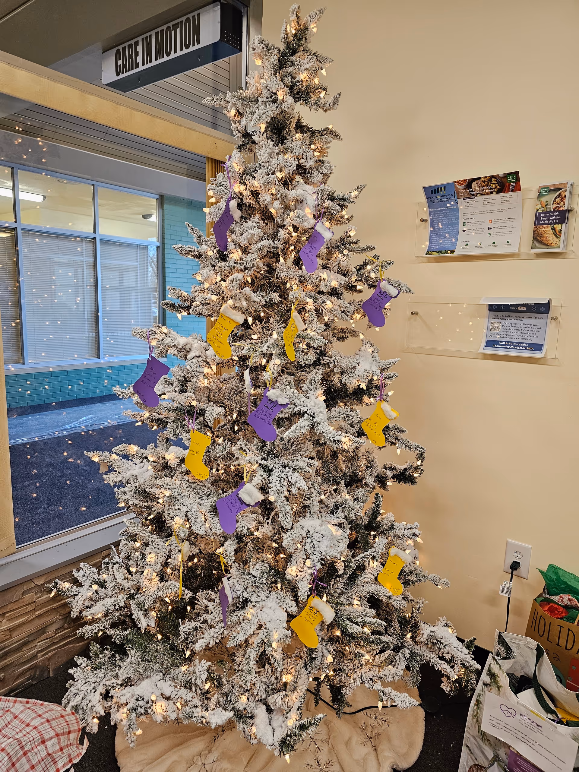 Snow-covered Christmas tree with lights stands in a lobby beside the Care In Motion sign.