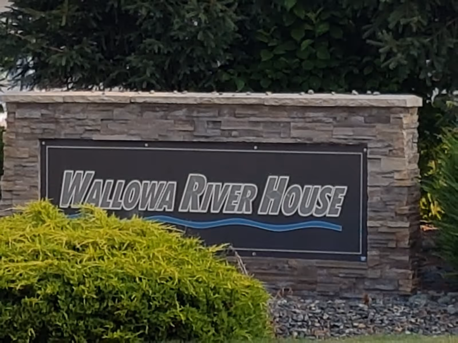 Stone sign reading Wallowa River House with shrubs in front.