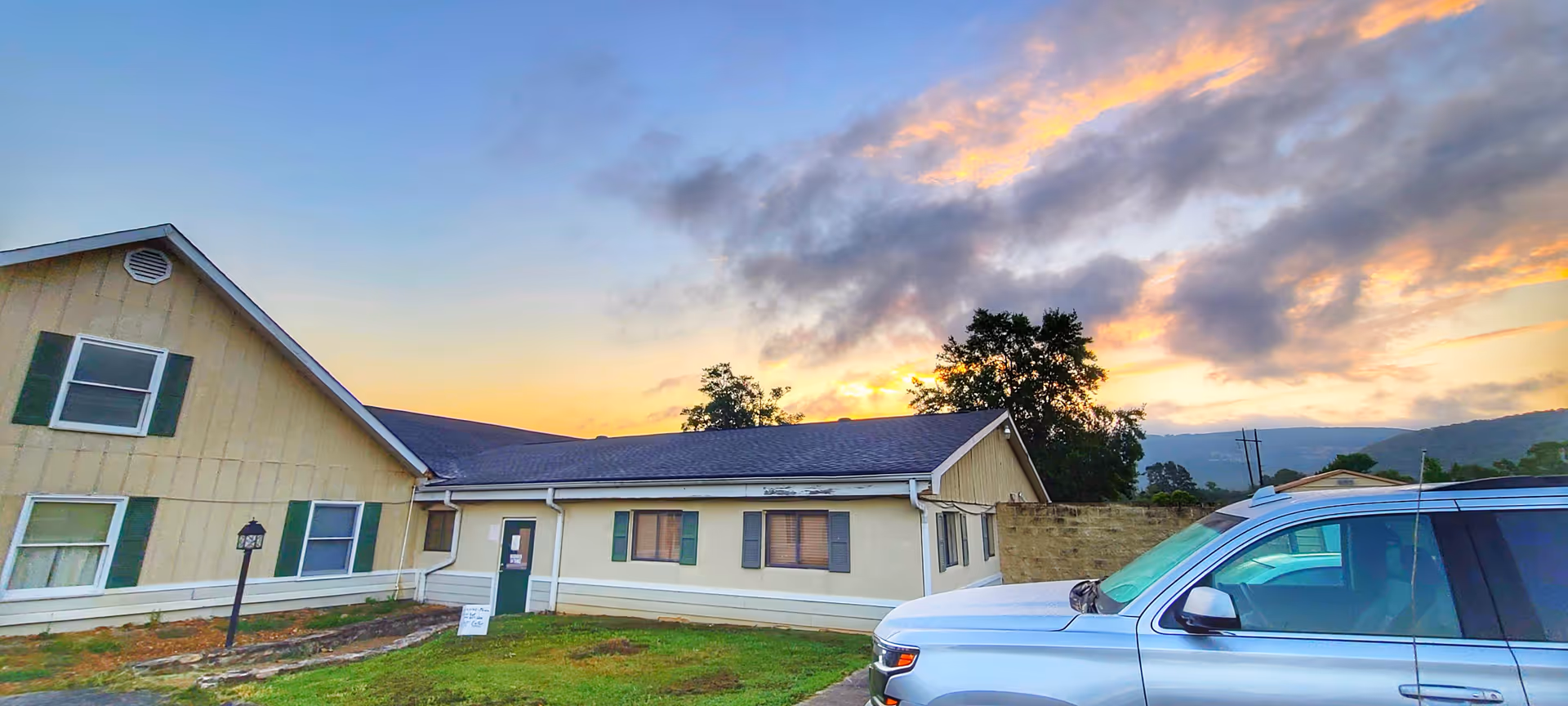 Exterior view of Woodhaven Personal Care facility with a parked silver SUV under a sunset sky.