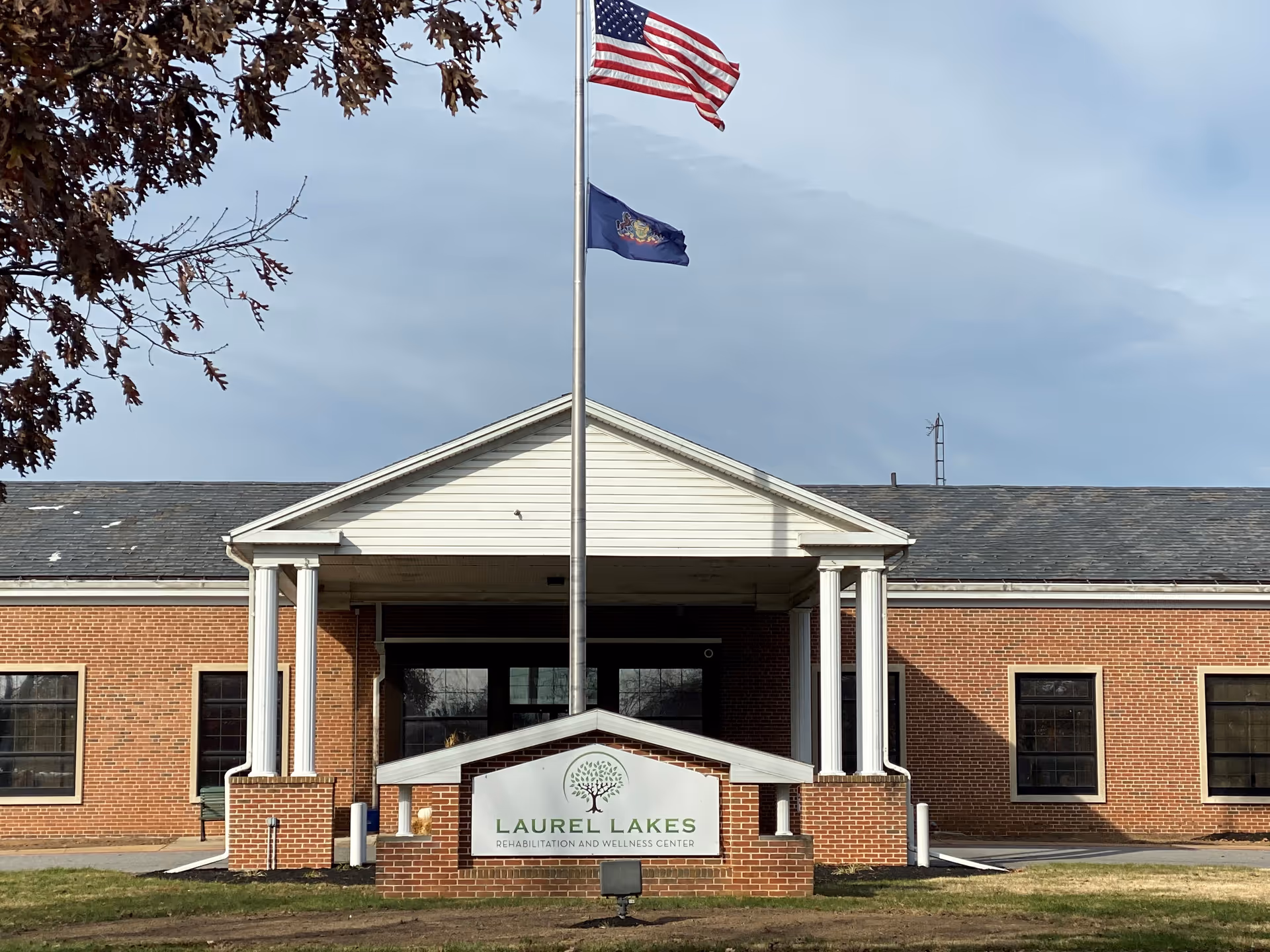 Brick building entrance with white portico and flagpoles in front.