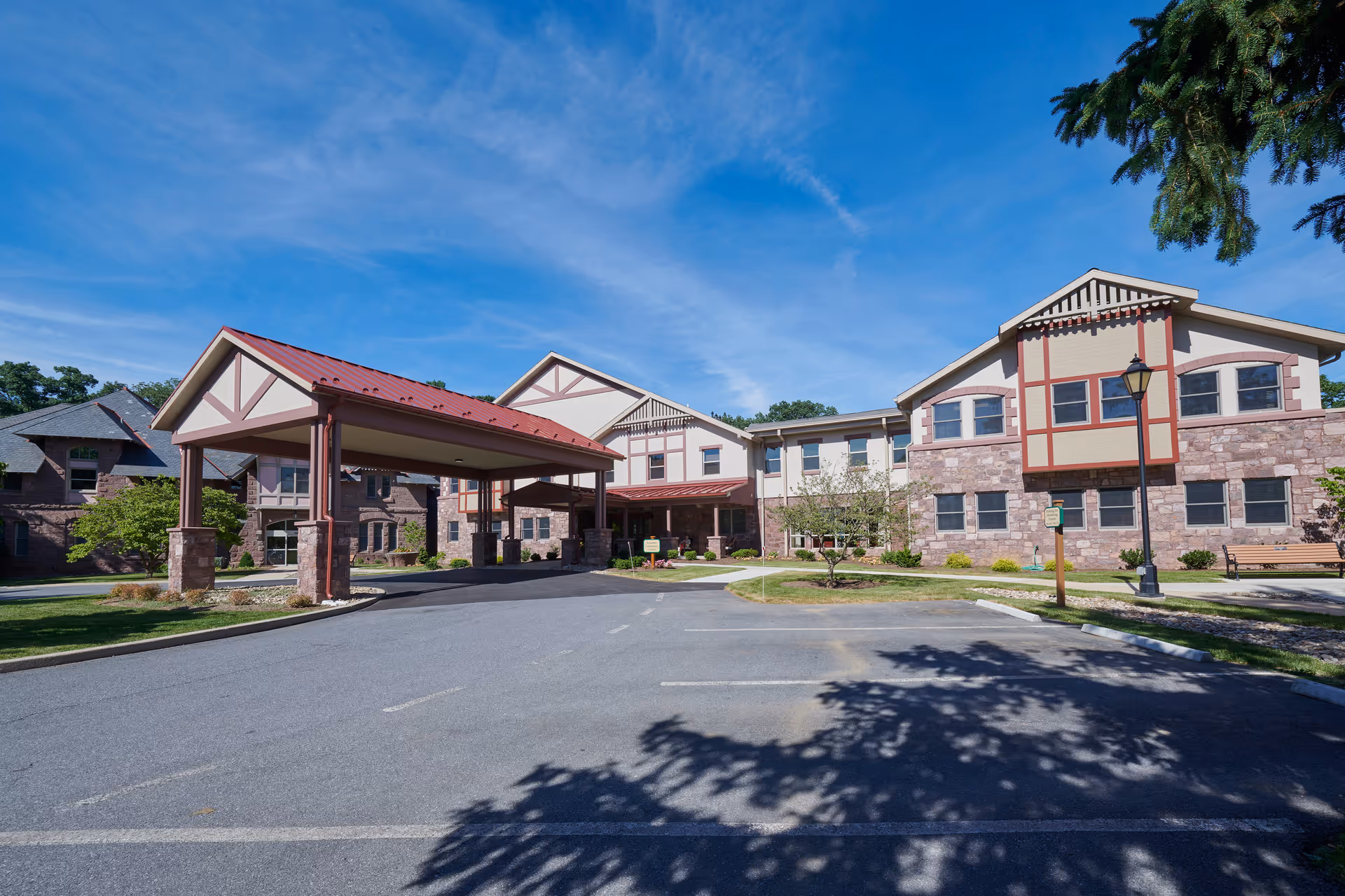 Front exterior of Cornwall Manor senior living building with a covered porte-cochere and parking area under a blue sky.