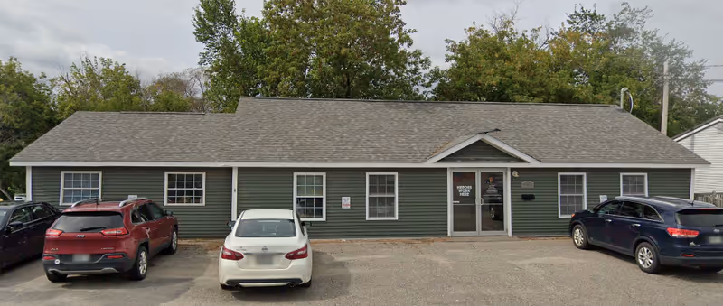 Single-story green building with front entrance and several cars parked in front.