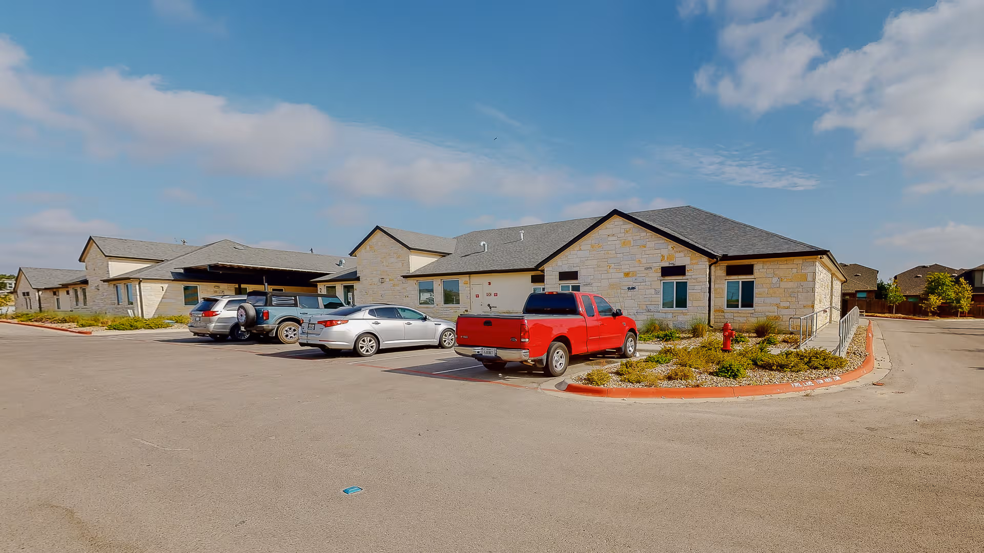 Exterior view of The Springs of Austin facility with stone walls, parking lot, and blue sky.
