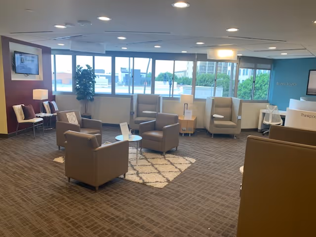Spacious senior living lounge with beige armchairs, small tables, rug, and large windows