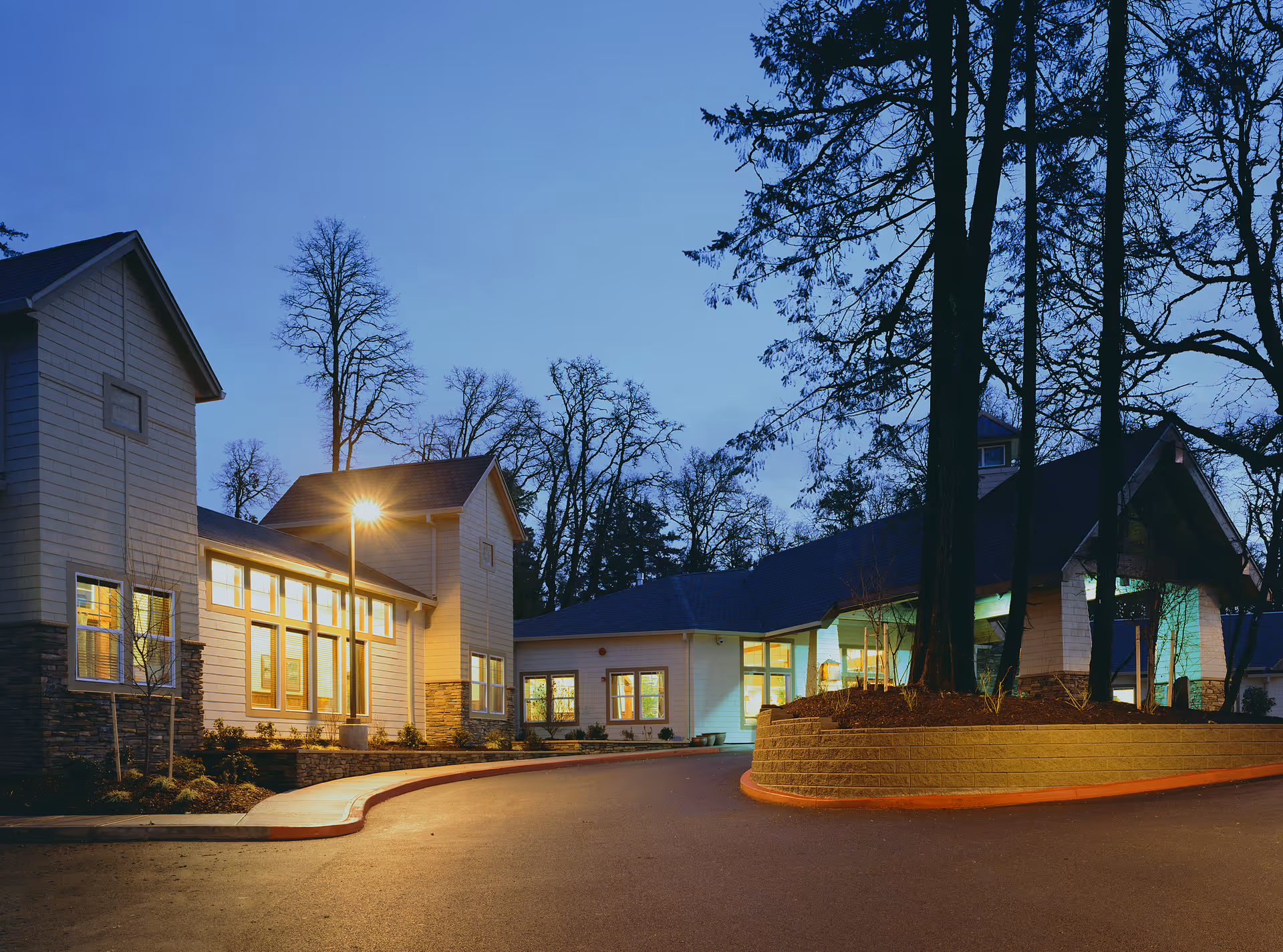 Evening exterior view of The Pearl at Kruse Way with illuminated entrance and curved driveway.