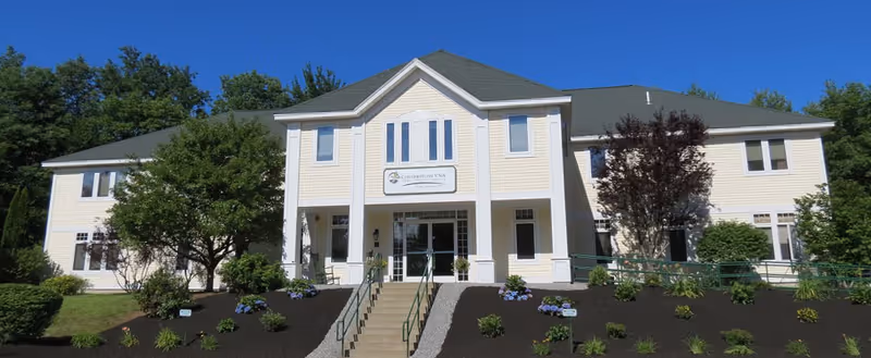 Two-story beige senior living facility with a central entrance and landscaped front yard.