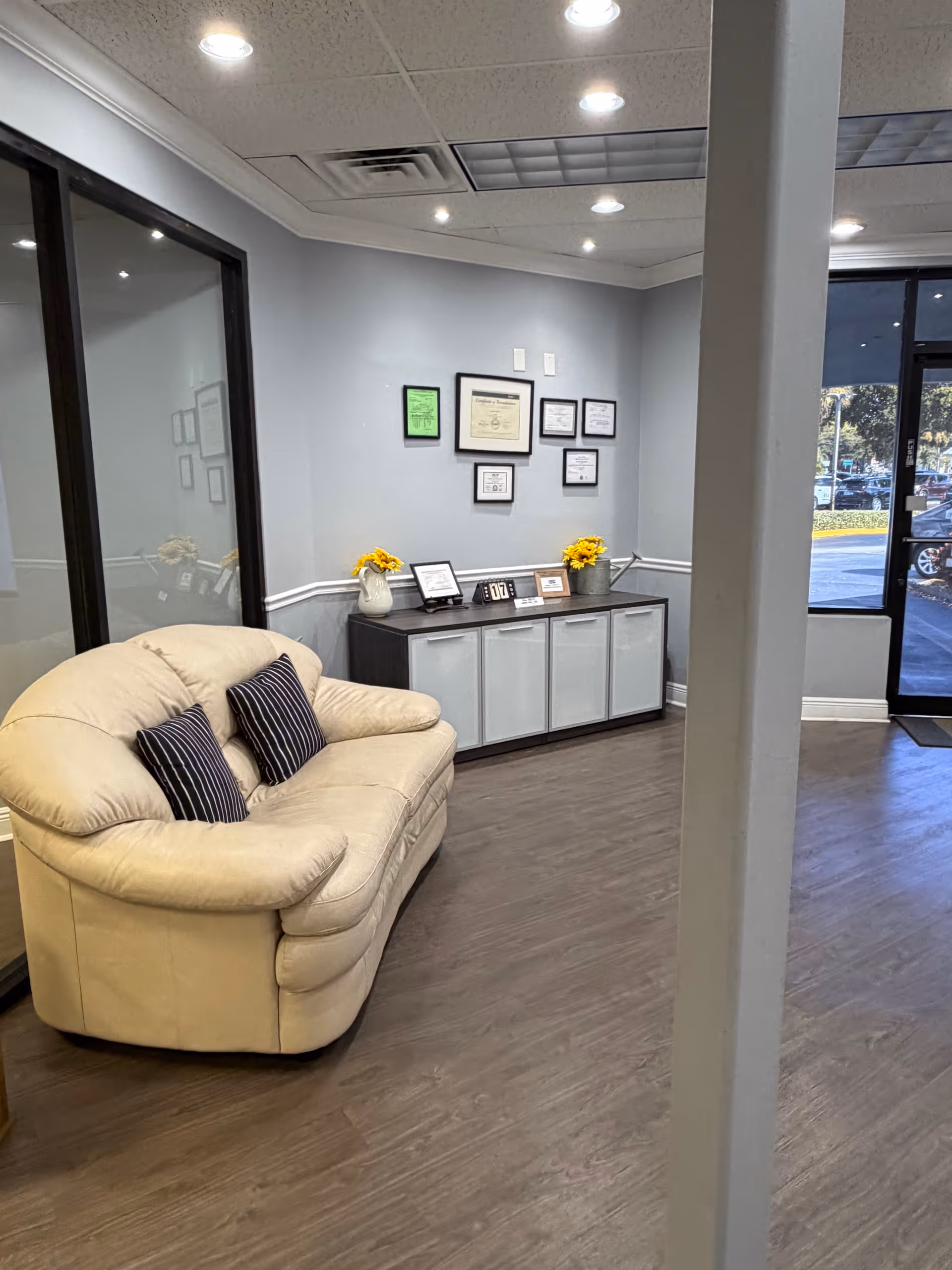 Beige sofa with striped cushions in a reception lobby beside a certificate wall.