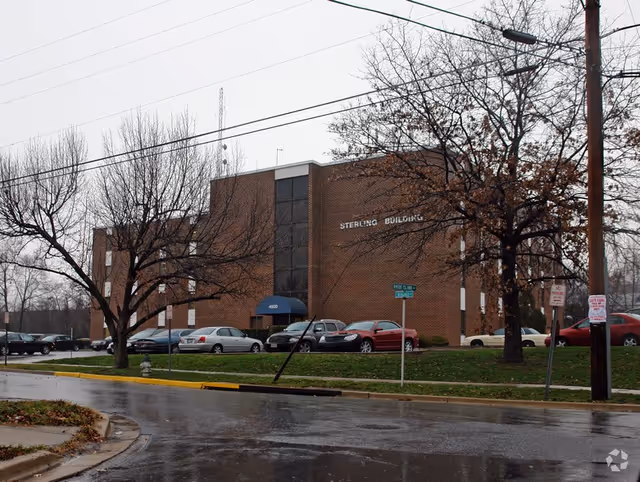 Exterior view of a brick building with parked cars along a wet street.