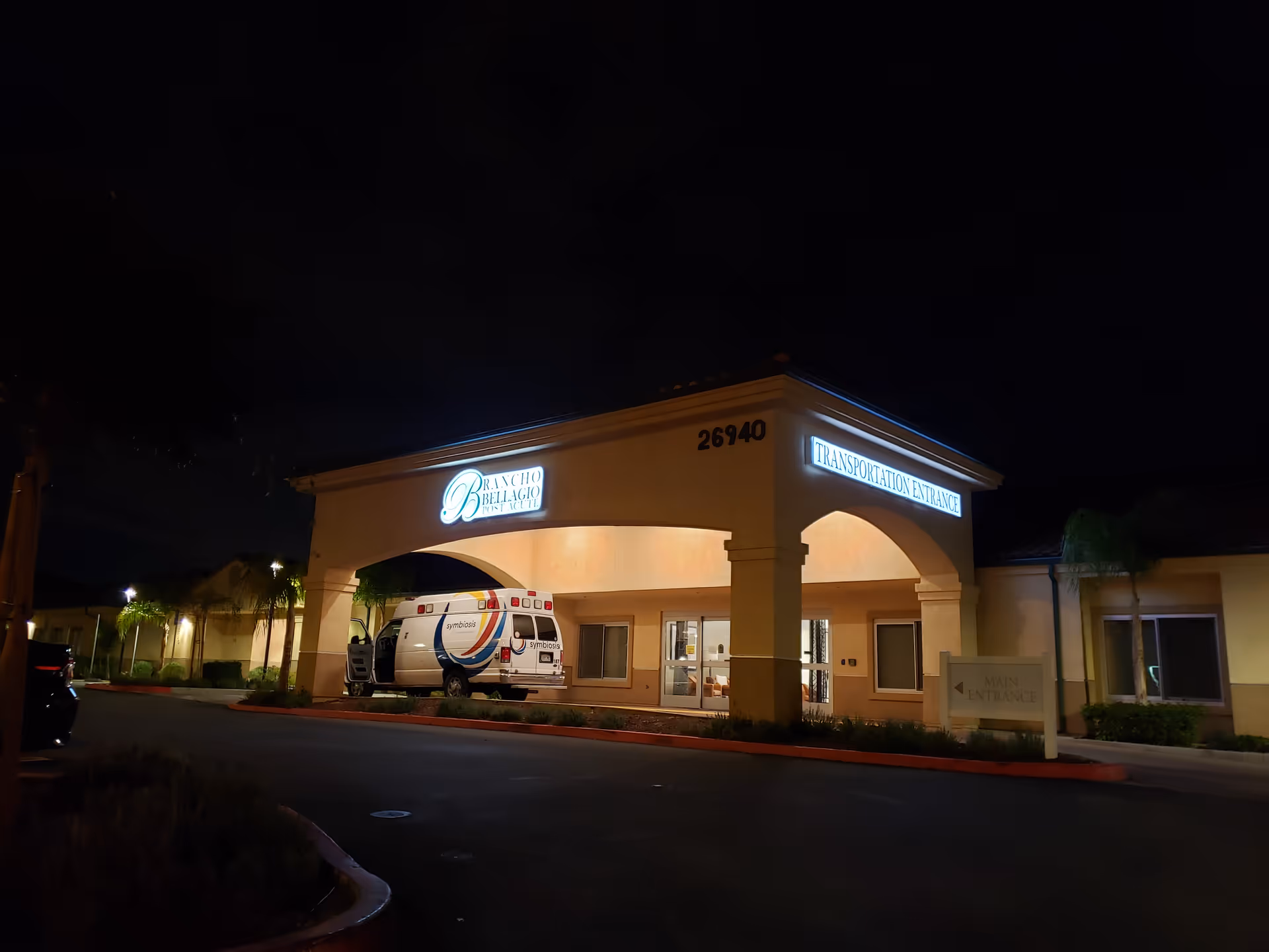 Night view of Rancho Bellagio Post Acute building entrance with a parked van.