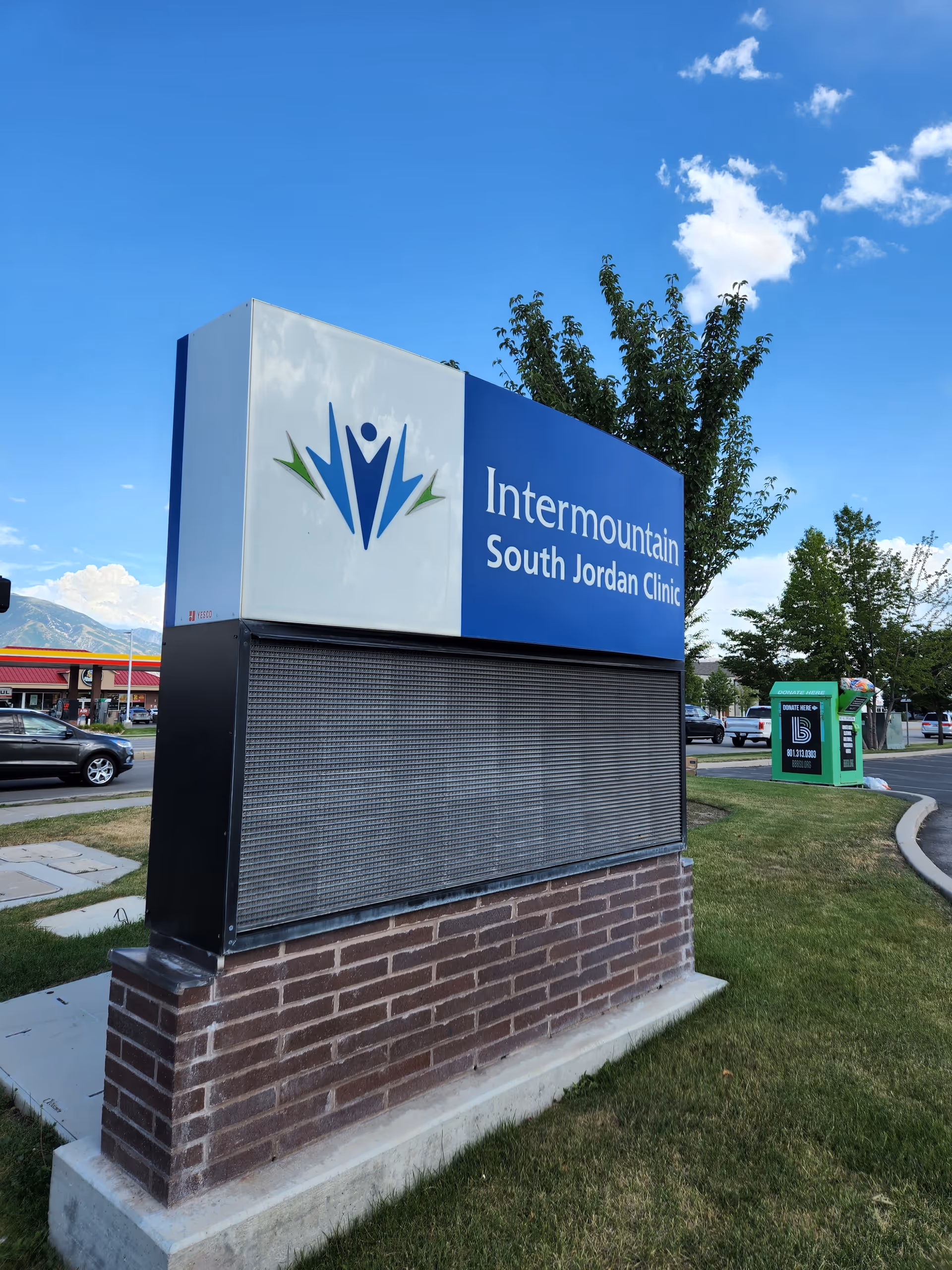 Exterior clinic sign reads Intermountain South Jordan Clinic, mounted on a brick pedestal near parking.