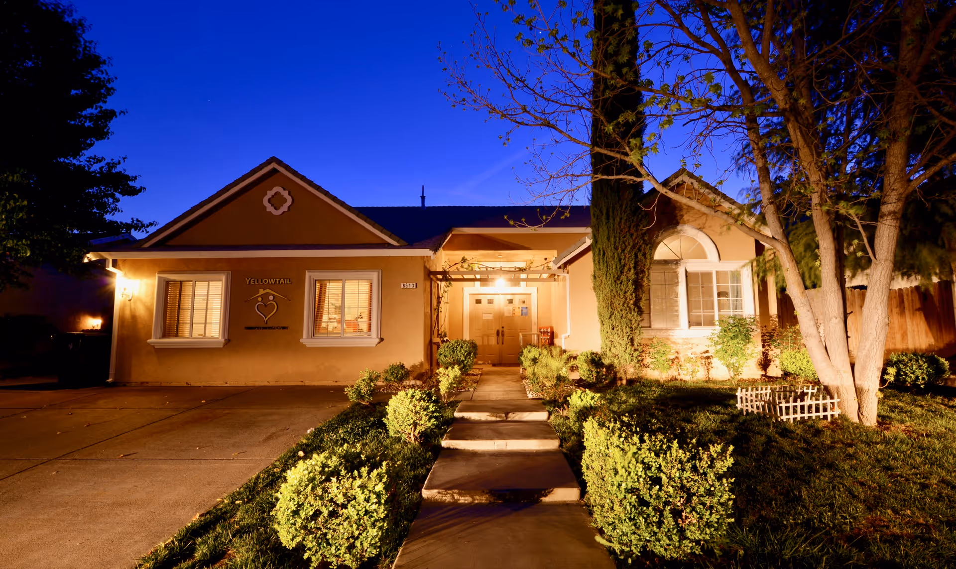 Night-time view of a warmly lit single-story senior living facility entrance.