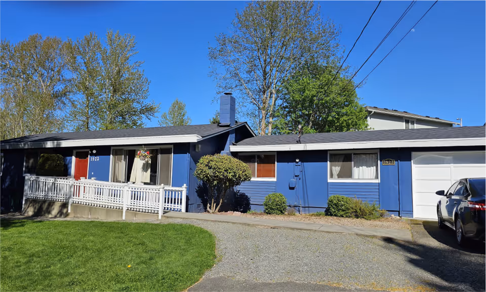 Blue single-story building with white railing, driveway, and a parked car on the right.