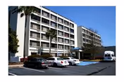 Two mid-rise buildings with balconies overlook a parking lot and palm trees.