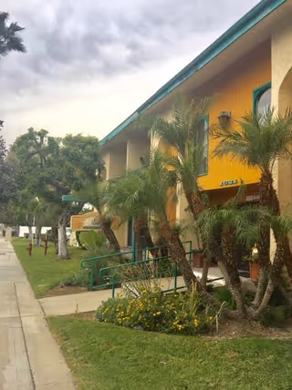 Exterior view of Cambridge Court Assisted Living building with yellow walls, green trim, and palm trees.