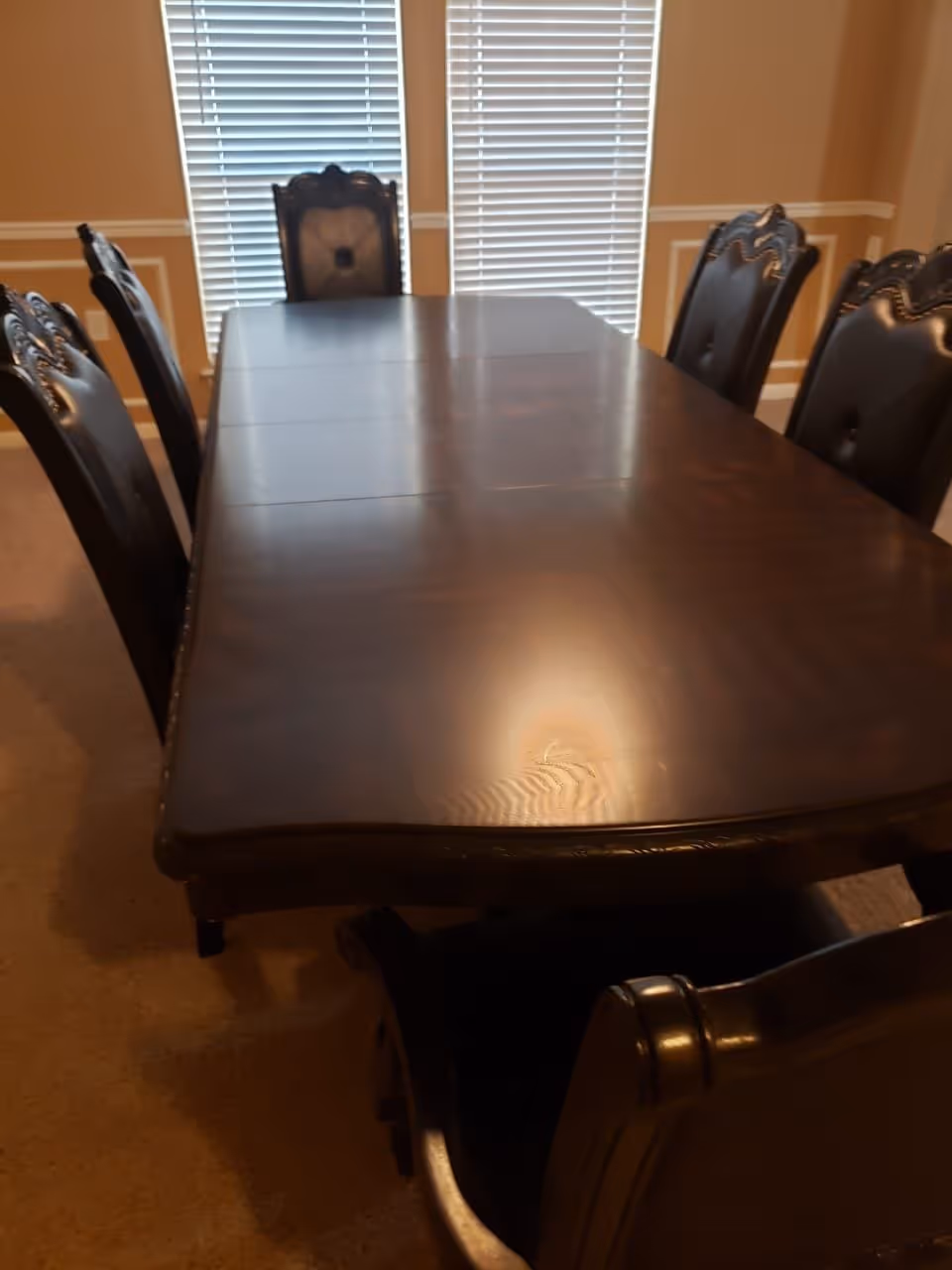 Long dark dining table with ornate chairs in a sunlit dining room.
