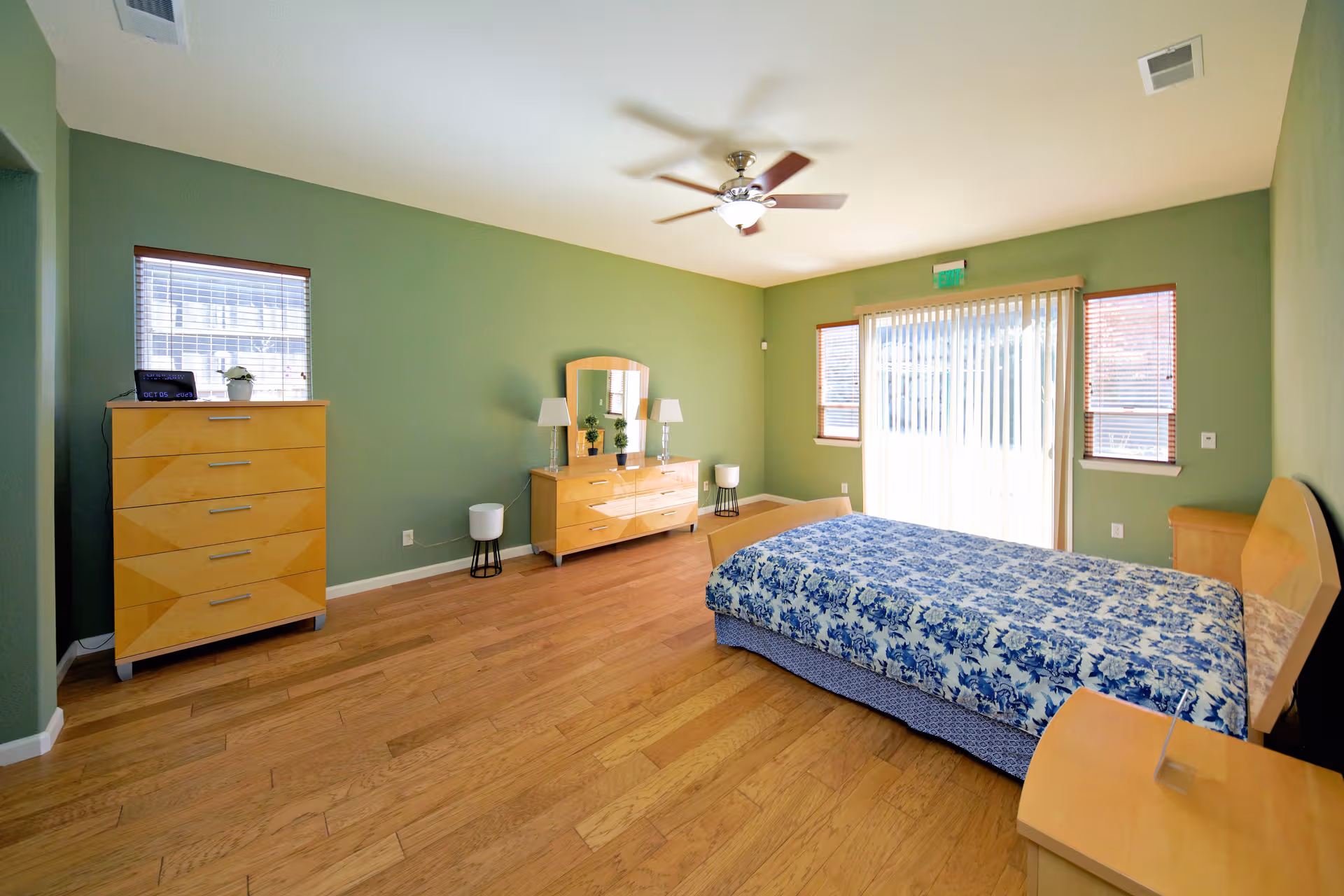 Spacious bedroom with wooden furniture, green walls, ceiling fan, and sliding glass door.