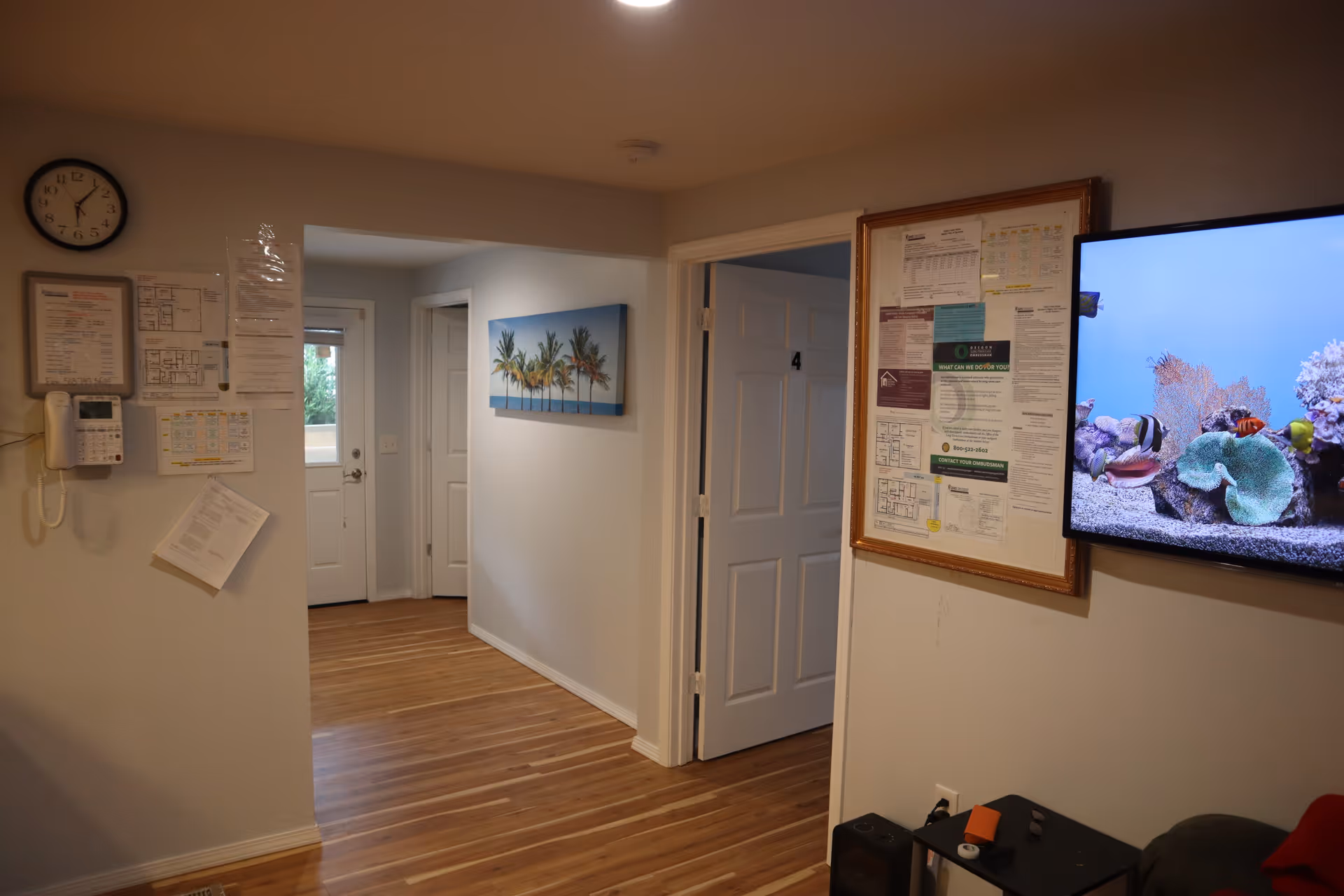 Interior hallway of Unity Adult Foster Care with bulletin boards, clock, and wall-mounted TV.