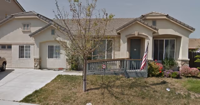 Front exterior of a single-story senior home with a ramp, flag, and landscaped yard.