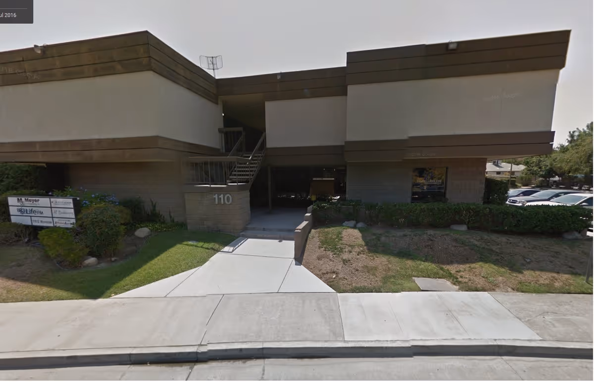 Exterior view of a low-rise building with stairs, entrance, and sidewalk in front.