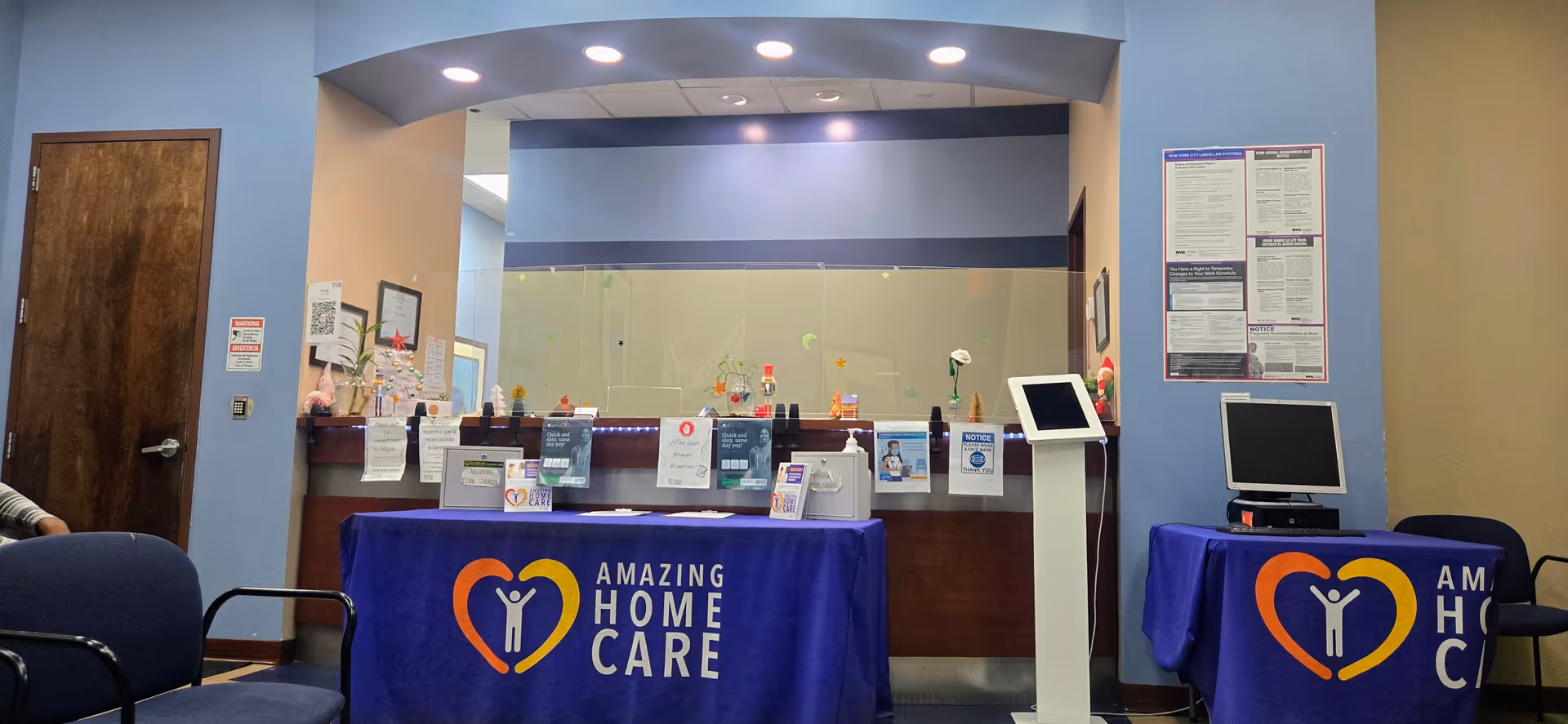 Reception area featuring a front desk with blue tablecloths, posters, and a standing kiosk.