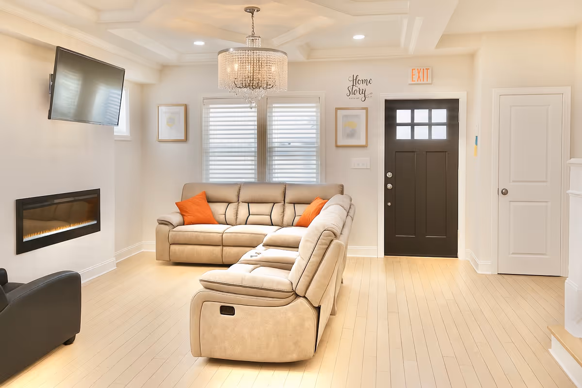 Bright modern living room with beige sectional, fireplace, TV, chandelier, and exit door.