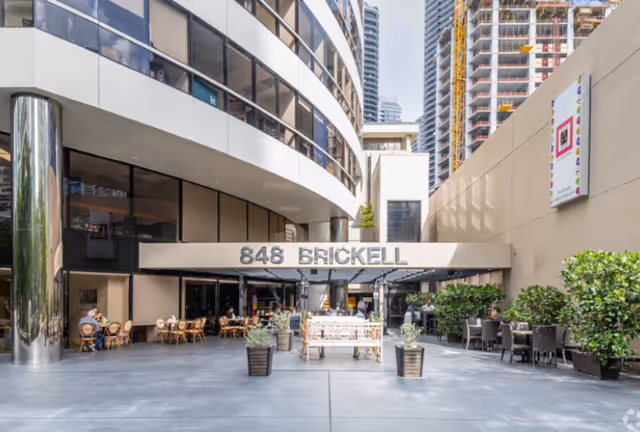 Outdoor dining area with tables and chairs in front of a modern building entrance.