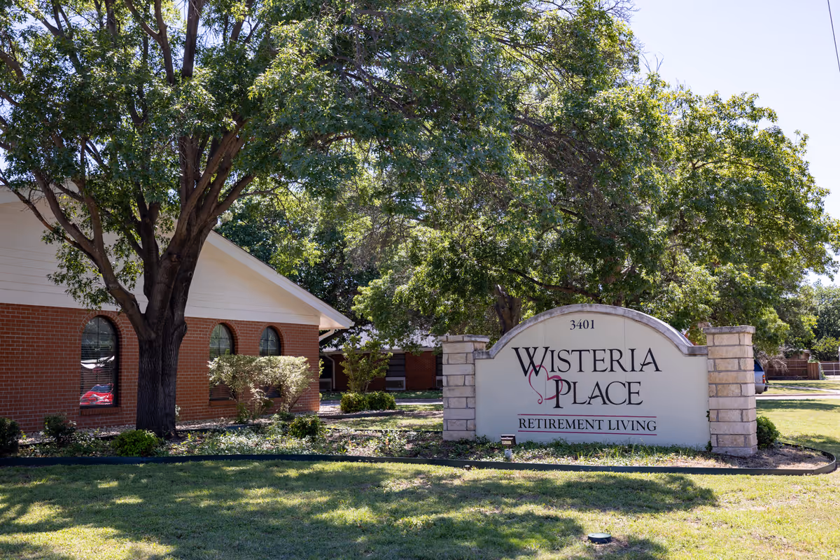Brick facility with arched windows and a large Wisteria Place sign in front yard.