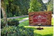 Outdoor scene with a brick Courtyard Assisted Living sign beside a grassy lawn and trees.