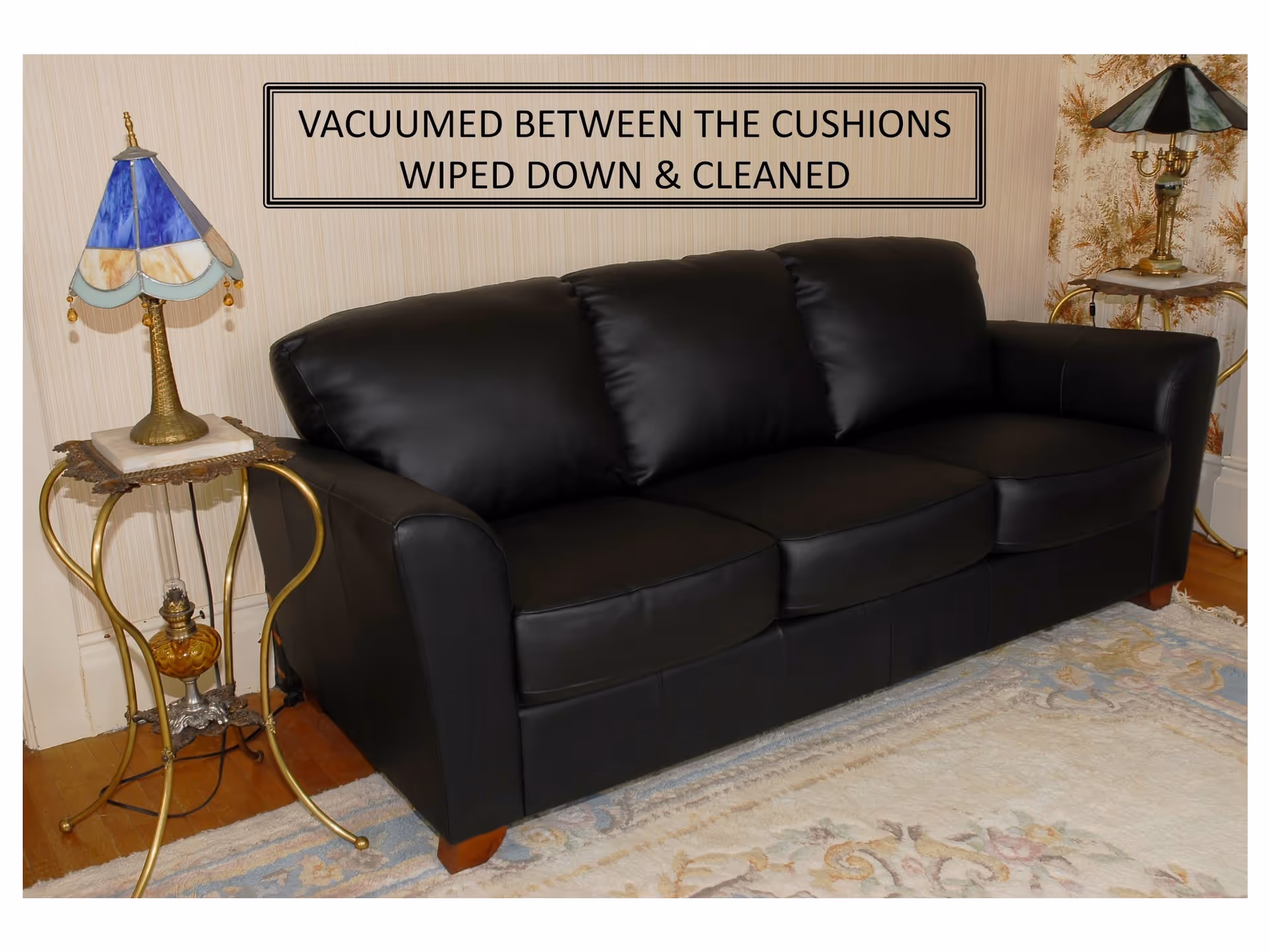 A black leather sofa in a living room with two ornate tables and lamps.